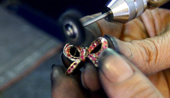 polissage-bijoux-artisanaux Le pendentif joaillerie "petit nœud" se trouve ici entre les mains de la polisseuse lui donnera tout son éclat. En or blanc, il est serti de saphirs roses et porté sur un collier en jaspe brun.