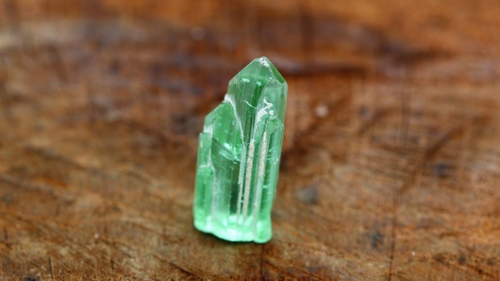 Rough tourmaline, copyright Arnoldi Lagoon green rough tourmaline on a wooden background.