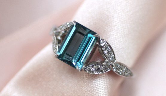 A Santa Maria africana aquamarine, emerald cut, adorns this white gold palladium center engagement ring. On each side, three leaves set with diamonds form the body of this women's ring.