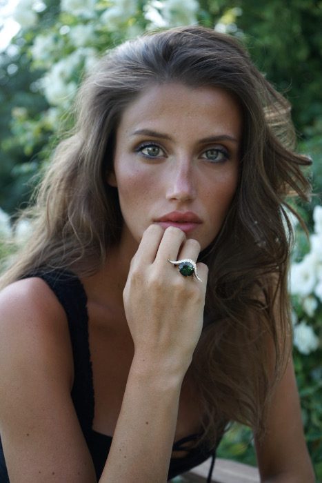 La bague "buffle", création de la joaillière Annette Girardon est portée par une jeune femme. Une ligne courbe, pavée de diamants contre laquelle s'appuie une tourmaline verte ronde forment la bague qui couvre presque 3 doigts.