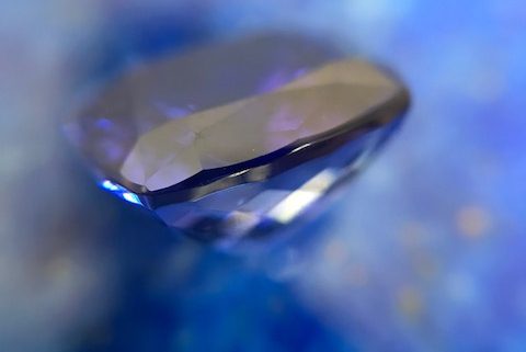 Une tanzanite en vue de profil contre du lapis lazuli, flou au fond, comme introduction d'un article traitant de la signification des pierres.