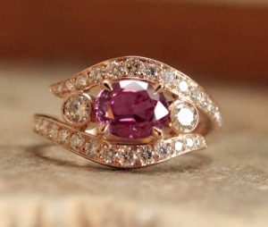 Résultat d'une transformation de bijou par un artisan joaillier créateur Cette bague femme en or rose dessinée sur-mesure, évoque la forme d'un oeil. Saphir rose ovale au centre accompagné de diamants.