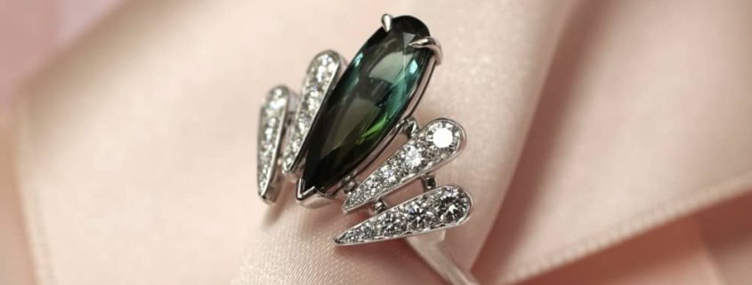 Cette bague de fiançailles originale évoque la plume d'un paon, avec sa toumaline bleue verte en forme de poire allongée au centre et accomagnée par des motifs pavés de diamants. C'est une création sur-mesure par la joaillière parisienne Annette Girardon.