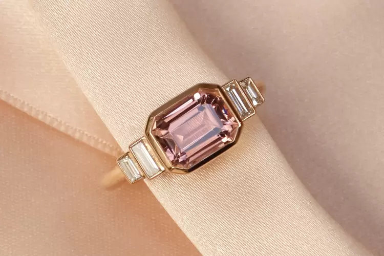 Cette bague, rappelant le style Art Déco est sertie d'une tourmaline rose clair, taille eméraude au centre, accompagnée de deux baguettes diamants.