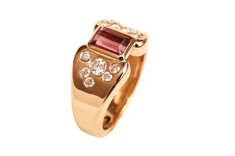 La bague en or rose forme un bandeau, ouvert au milieu. Le lien est fait par une tourmaline rose. Sur les côtés, des diamants sont sertis dans de l'or rose.