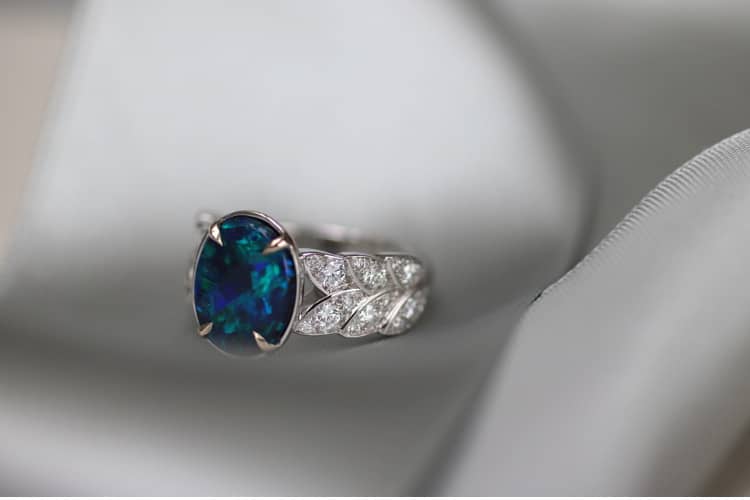 Le corps de cette bague est en forme bandeau, constitué de feuilles pavées de diamants. Au centre, une opale noire d'Australie ovale nous envoute avec ses reflets d'un camaïeu de bleus.