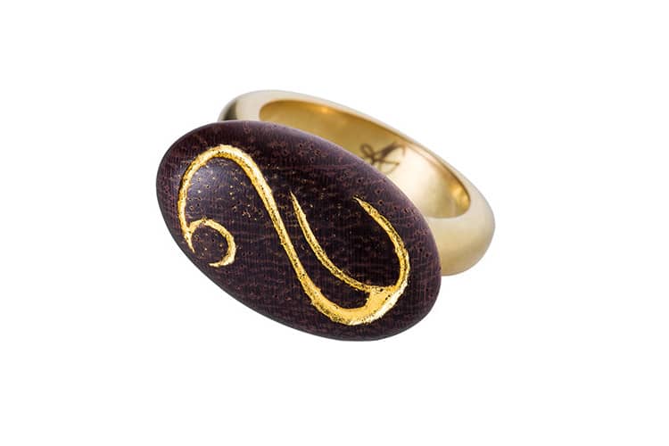 Une bague en bois exotique, or 22 carat et portant une gravure, dorée à la feuille d'or. Il s'agit d'une création de bijou rare, par Annette Girardon, installée à Paris.