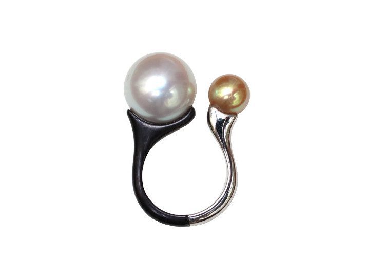Une grande perle blanche et une plus petite perle gold sont posées sur deux branches, noire et blanche, qui forment le corps de la bague.