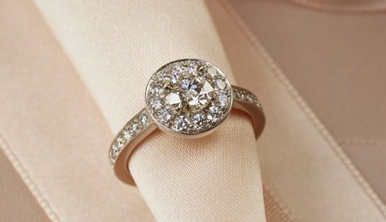 bague-entouree-de-diamants Cette bague de fiançailles en or blanc palladié est sertie d'un brillant, entouré d'un halo de diamants. Le corps de bague au profil carré est également orné de petits diamants.
