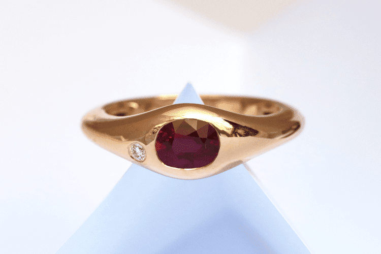 Bague homme rubis rouge et diamant Un rubis ovale d'un beau rouge est serti dans cette bague homme personnalisée. La bague est en or rouge, de forme simple et fluide, qui s'élargit au mileu.