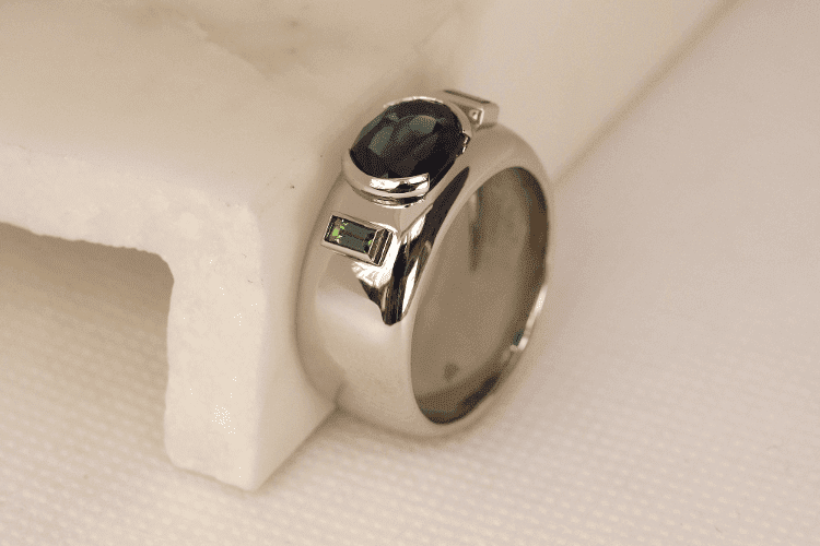 Bague pour homme Paris Un saphir ovale et deux baguettes tsavorite sont sertis sur cette bague pour homme luxe en forme bandeau. Elle a été créée à Paris, sur-mesure.