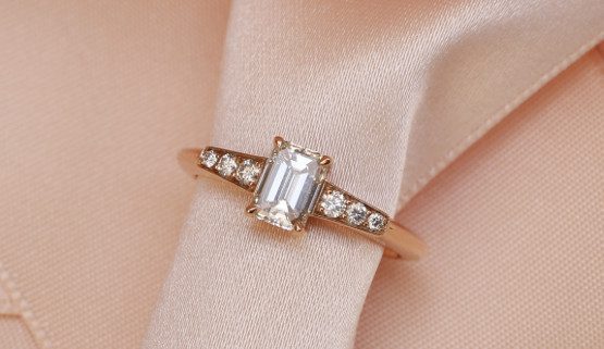 Bague de fiançaille avec diamant taille émeraude Un diamant taille émeraude de 0.7 ct est épaulé de deux motifs en forme trapèze, pavé de diamants sur or rouge. Cette bague de fiançailles élégante et équilibrée a été dessinée par la joaillière Annette Girardon à Paris.