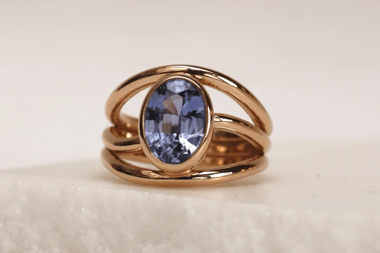 Trois anneaux fluides en or rouge 18 carat forment le corps de cette bague d'envergure. Un saphir ovale violet en serti clos se trouve au centre.