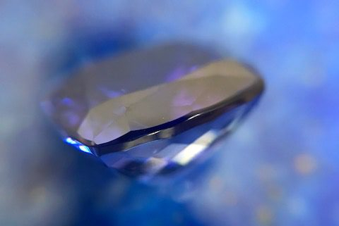 Ein Tansanit Stein ist im Profil vor einem Lapislazuli abgebildet, welcher in unscharfer Form den Hintergrund füllt.