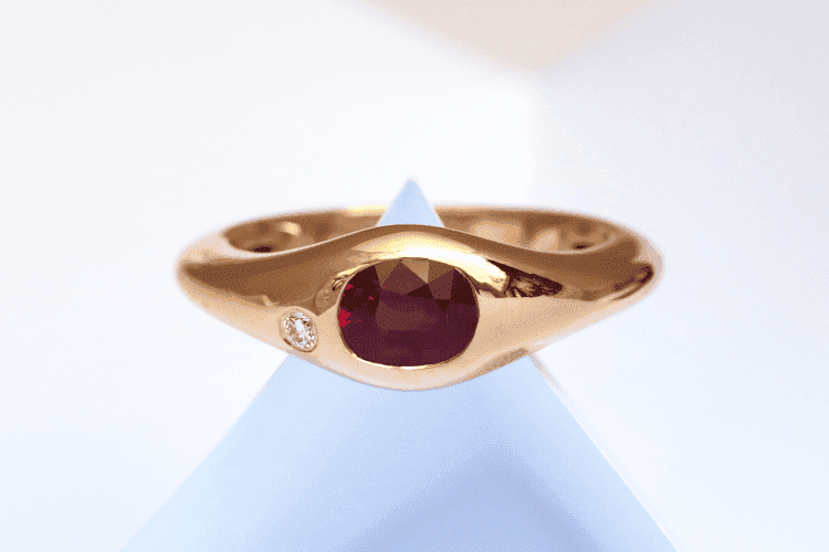 handmade-men's-ring A beautiful red oval ruby is set in this personalized men's ring. The ring is made of red gold, with a simple, flowing shape that widens in the middle.