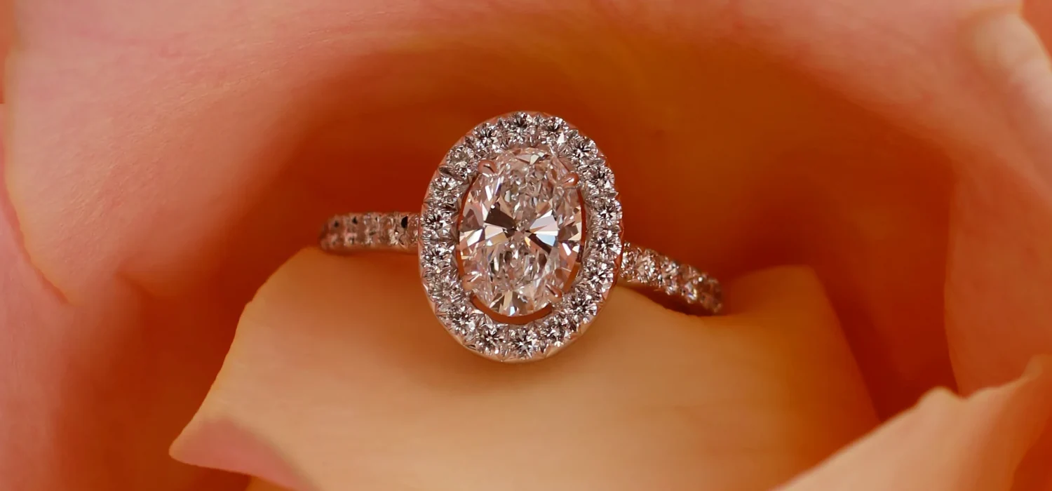 Bague de fiançailles sur mesure avec diamant taille ovale, entouré d'un halo de petits diamants.